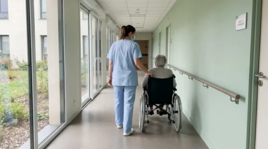 Soignante accompagnant une personne âgée dans un couloir d